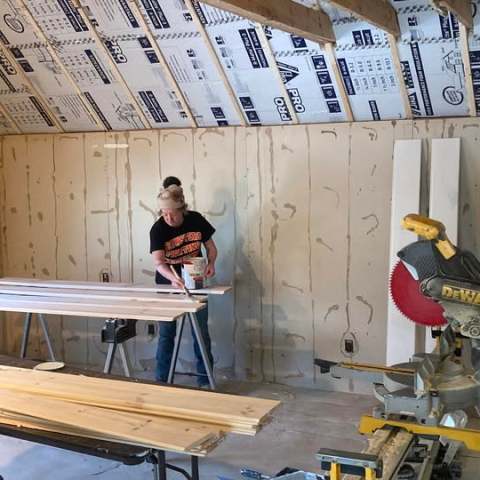 Person working on wood planks in a room under construction, with tools and insulation visible.