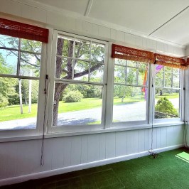 Enclosed sunroom with large windows and green carpet overlooking a grassy yard.