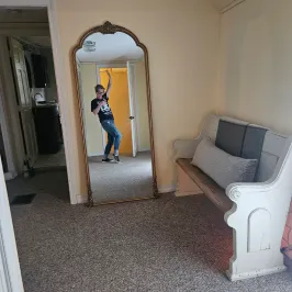 Person in mirror posing in room with bench and doorway.