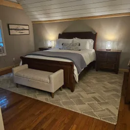 Cozy bedroom with wooden bed, white bedding, rug, nightstands, and two lamps.