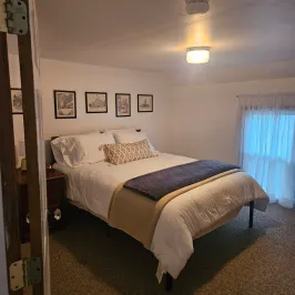 Cozy bedroom with neatly made bed, framed pictures, and a small window.