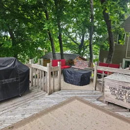 Wooden deck with BBQ, tables, and leafy trees surrounding.