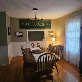 Dining room with a wooden table, six chairs, and a sign reading 'Betts Bookstore' on the wall.